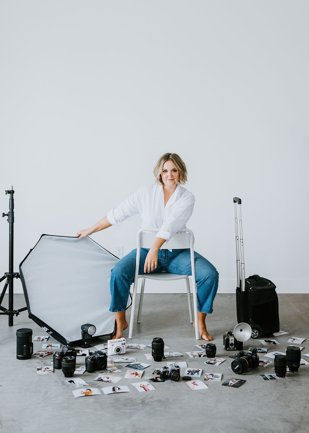 Maddie Peschong sitting in a white studio in front of a white wall with all her camera gear around her.